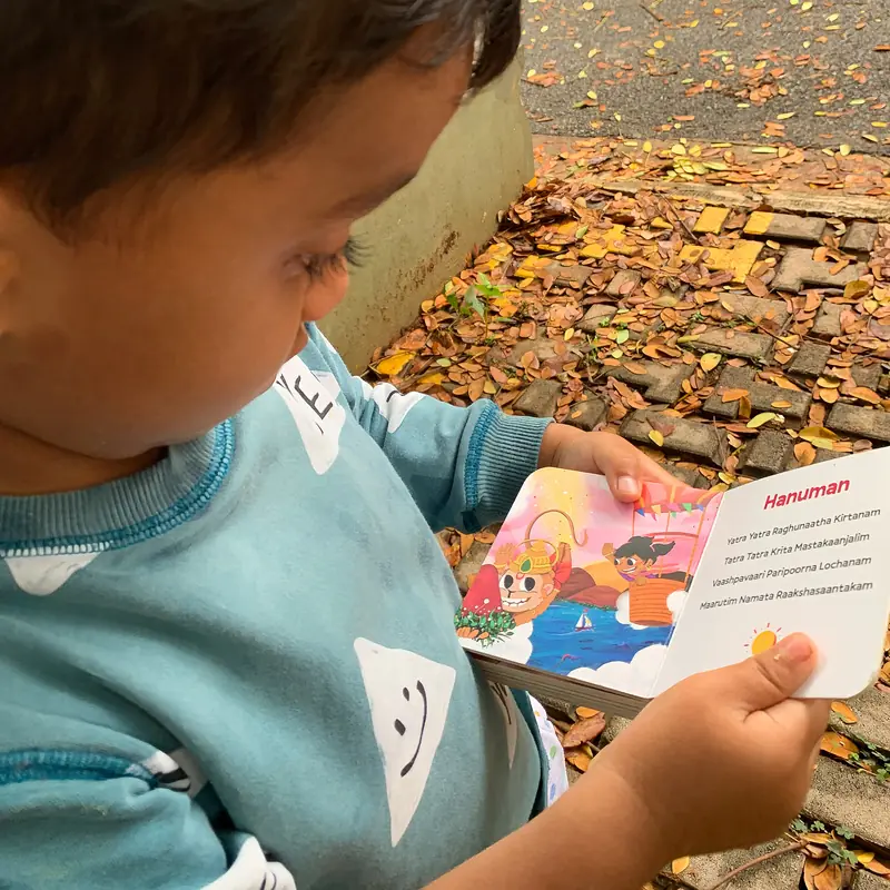 Dhruva sitting on a doorstep, reading the Hanuman spread of Oh My Gods on his own