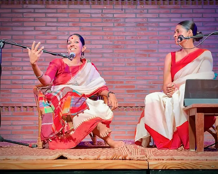 Priya on stage, telling a story into a microphone beside a fellow performer
