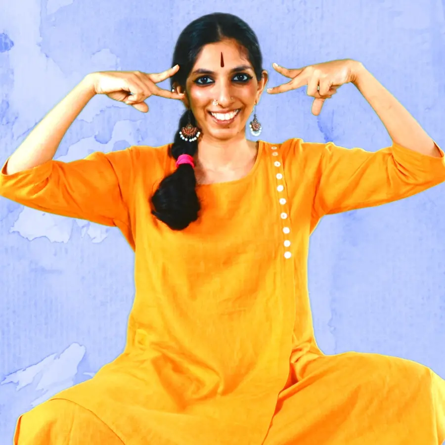 Priya smiling, both index fingers pointing at her temples