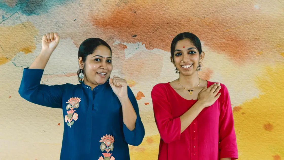 Varsha, in blue with a fist raised, and Priya, in pink with a hand on her heart, smiling on a watercolour wash.